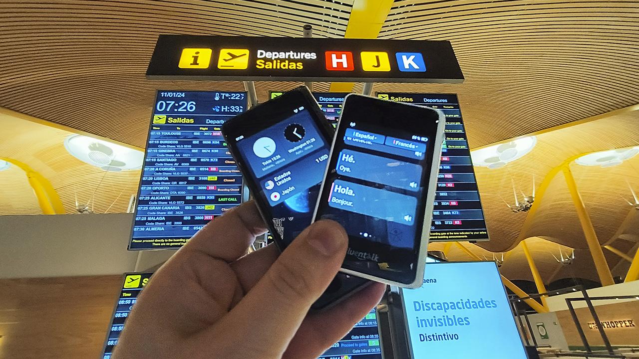 dos traductores digitales frente a un panel de aeropuerto