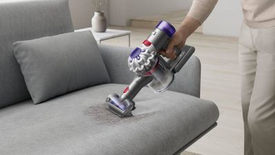 Persona utilizando una aspiradora de mano inalámbrica para limpiar la tapicería de un sofá.