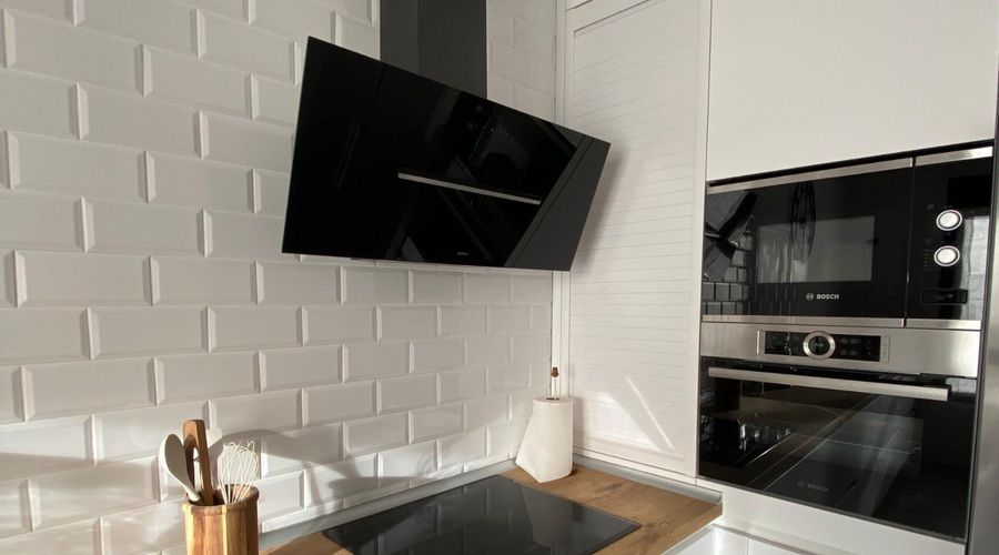Campana extractora decorativa negra de diseño inclinado, instalada en una cocina moderna con muebles blancos y encimera de madera