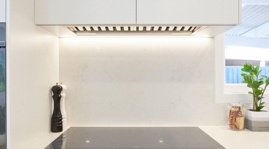 Campana extractora integrada en un mueble blanco de cocina, instalada sobre una placa de inducción