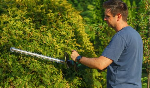 Hombre utilizando un cortasetos inalámbrico para podar un seto en un jardín