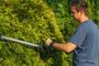 Hombre utilizando un cortasetos inalámbrico para podar un seto en un jardín