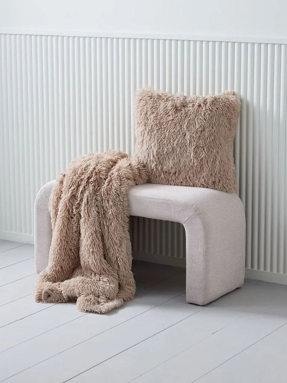 Cojín y manta de pelo en tonos beige colocados sobre una silla en un ambiente de estilo acogedor.
