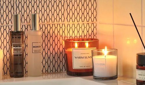 Velas aromáticas encendidas y ambientador con varillas decorando un baño con una iluminación cálida.