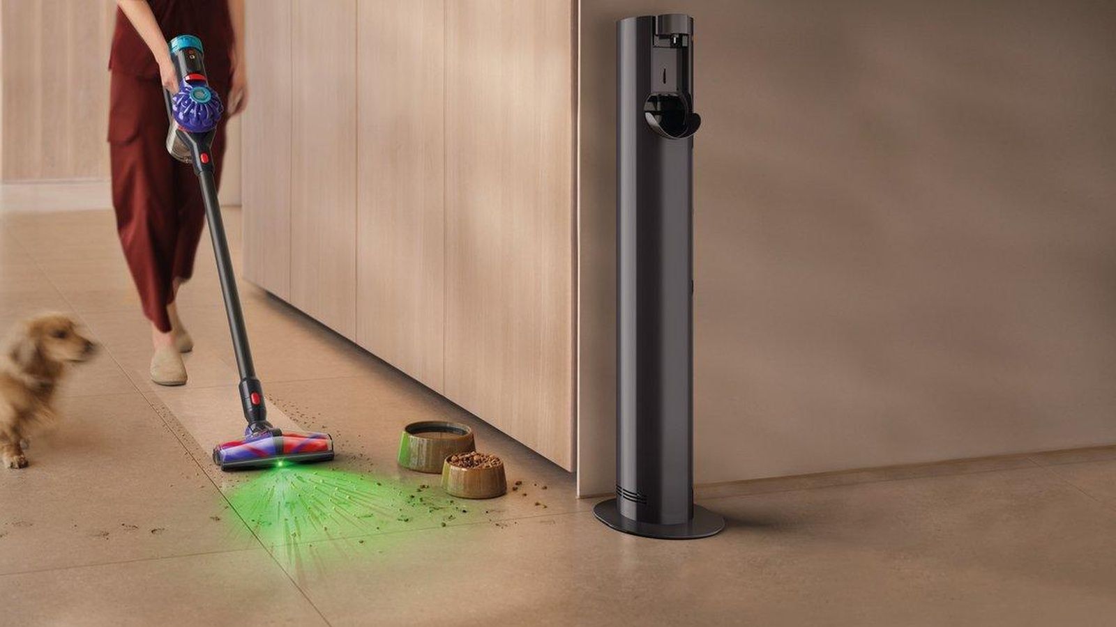 Persona utilizando una aspiradora Dyson V10 Konical para limpiar el suelo junto a un perro y varios restos de comida.