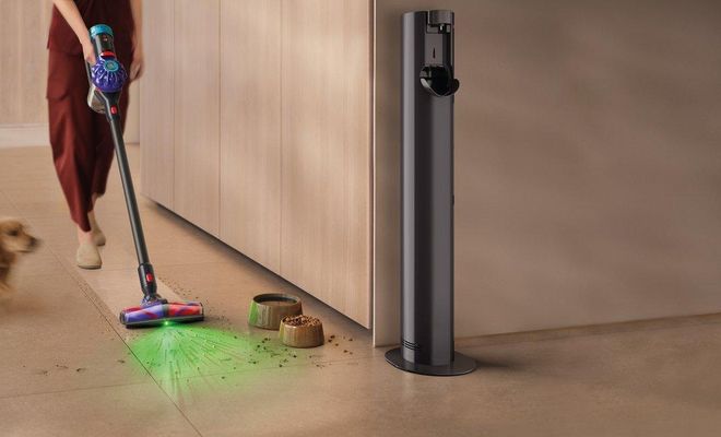 Persona utilizando una aspiradora Dyson V10 Konical para limpiar el suelo junto a un perro y varios restos de comida.