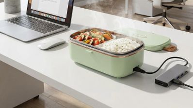 Fiambrera eléctrica con comida caliente sobre una mesa de oficina junto a un ordenador portátil