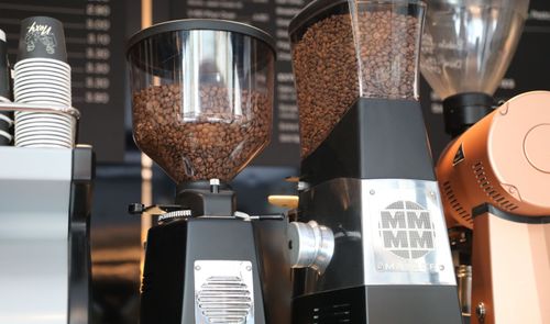 Molinillos de café profesionales con depósitos llenos de granos de café en una cafetería.