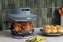 Freidora de aire Ninja CRISPi PRO XL con recipiente de cristal cocinando un pollo junto a otro recipiente con pan.