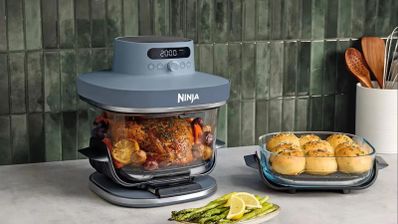 Freidora de aire Ninja CRISPi PRO XL con recipiente de cristal cocinando un pollo junto a otro recipiente con pan.