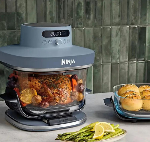 Freidora de aire Ninja CRISPi PRO XL con recipiente de cristal cocinando un pollo junto a otro recipiente con pan.
