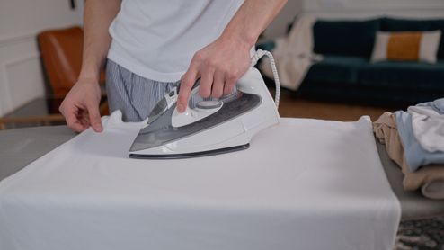 Hombre utilizando una plancha de vapor para planchar una camisa blanca sobre una tabla de planchar.