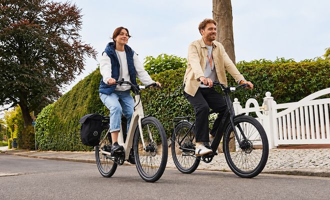 Dos personas circulando en bicicletas eléctricas negras por una calle residencial