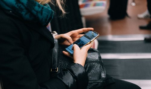 Mujer utilizando un teléfono móvil mientras espera en una zona pública rodeada de otras personas