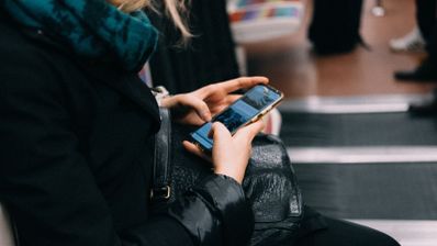 Mujer utilizando un teléfono móvil mientras espera en una zona pública rodeada de otras personas