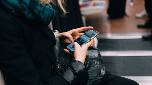 Mujer utilizando un teléfono móvil mientras espera en una zona pública rodeada de otras personas