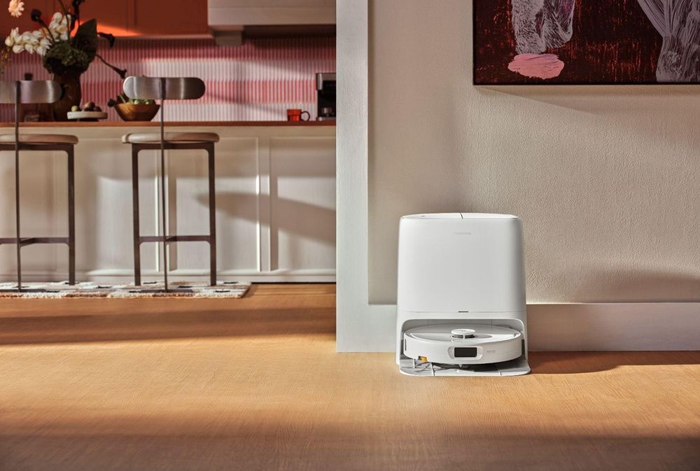 Robot aspirador Roborock blanco situado en su estación de carga junto a una cocina.