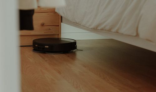 Robot aspirador negro limpiando el suelo de un dormitorio y accediendo a la zona situada debajo de la cama