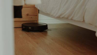 Robot aspirador negro limpiando el suelo de un dormitorio y accediendo a la zona situada debajo de la cama