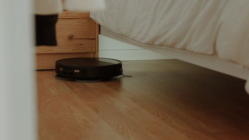 Robot aspirador negro limpiando el suelo de un dormitorio y accediendo a la zona situada debajo de la cama