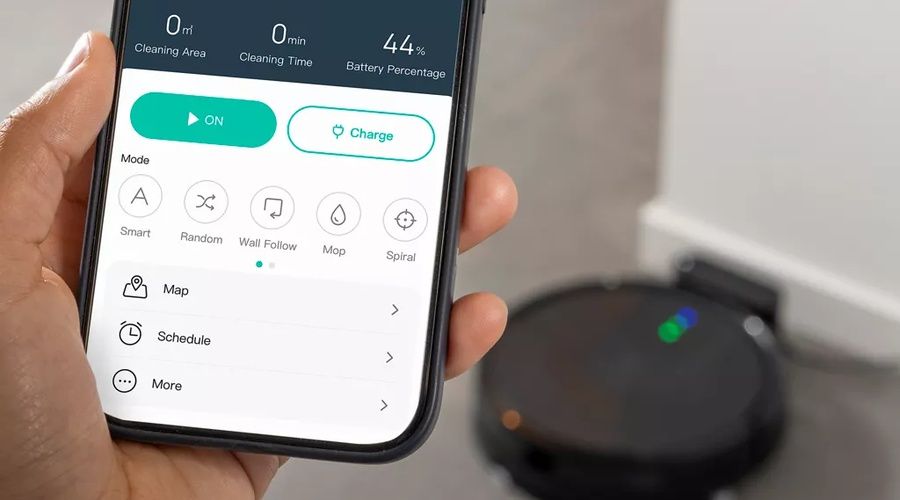 Persona controlando un robot aspirador desde una aplicación móvil mientras el dispositivo permanece junto a su base de carga