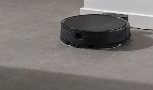 Robot aspirador negro limpiando el suelo de una vivienda junto a su base de carga