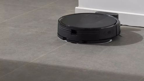 Robot aspirador negro limpiando el suelo de una vivienda junto a su base de carga