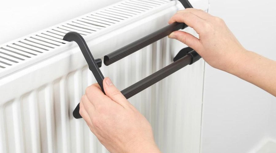 Persona instalando un tendedero extensible negro sobre un radiador blanco
