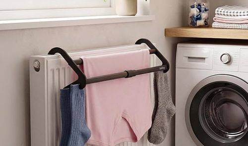 Tendedero extensible acoplado a un radiador blanco con varias prendas colgadas junto a una lavadora