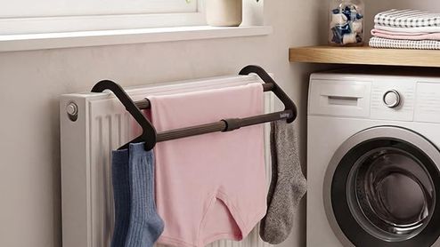 Tendedero extensible acoplado a un radiador blanco con varias prendas colgadas junto a una lavadora