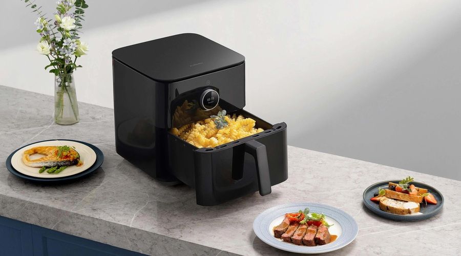 Freidora de aire Xiaomi negra con la cesta abierta y patatas fritas, acompañada de varios platos preparados sobre una encimera