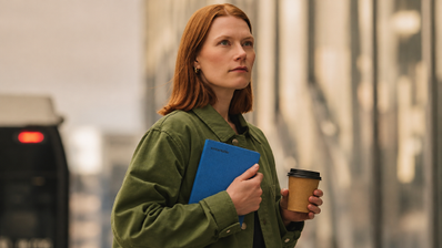 Mujer sosteniendo un reMarkable Paper Pro Move con funda azul mientras lleva un café en la mano.