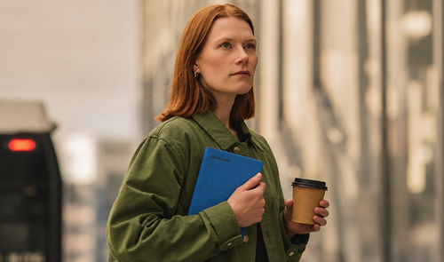 Mujer sosteniendo un reMarkable Paper Pro Move con funda azul mientras lleva un café en la mano.