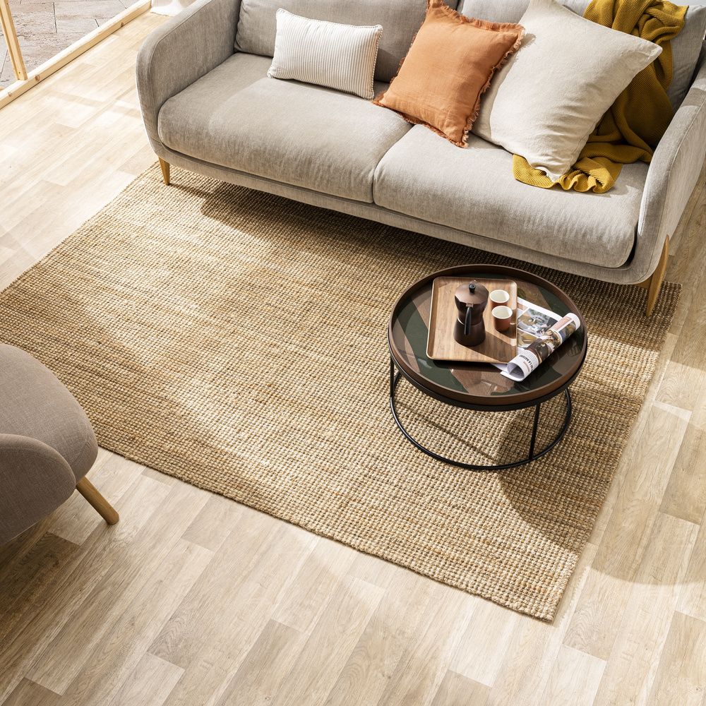 Alfombra rectangular de yute bajo una mesa de centro redonda y frente a un sofá con cojines de tonos neutros.