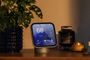 Apple HomeView sobre un mueble de madera, junto a una planta y varios objetos decorativos, con controles del hogar en pantalla.