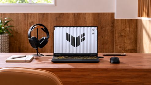 ASUS TUF Gaming F16 abierto sobre un escritorio de madera, junto a unos auriculares y un ratón.