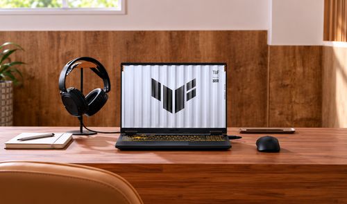 ASUS TUF Gaming F16 abierto sobre un escritorio de madera, junto a unos auriculares y un ratón.