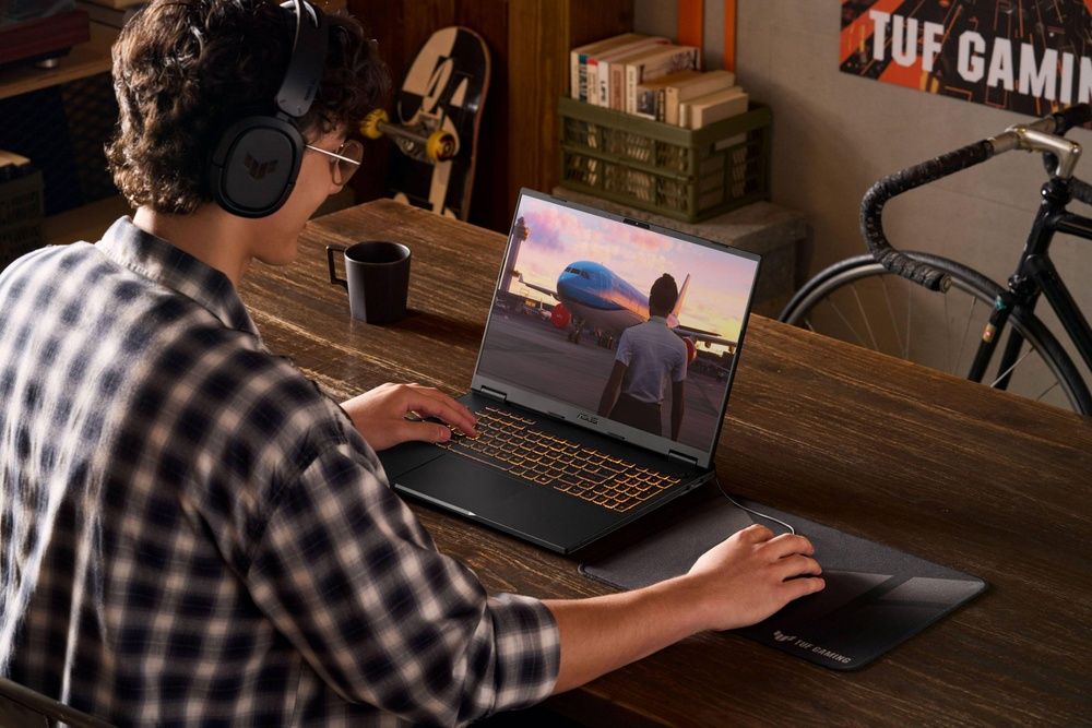 Persona con auriculares jugando en un ASUS TUF Gaming F16 sobre una mesa de madera.