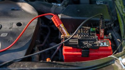 Batería de coche con pinzas rojas y negras conectadas en el compartimento del motor.