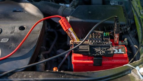 Batería de coche con pinzas rojas y negras conectadas en el compartimento del motor.