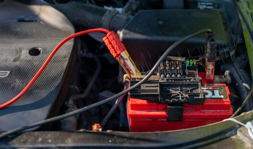 Batería de coche con pinzas rojas y negras conectadas en el compartimento del motor.