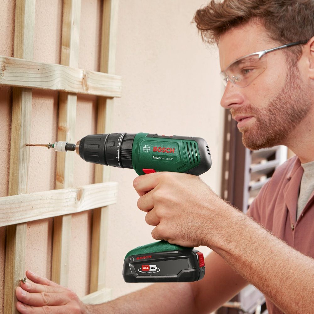 Hombre con gafas de protección utilizando un Bosch EasyImpact 18V-40 para introducir un tornillo en una estructura de madera.