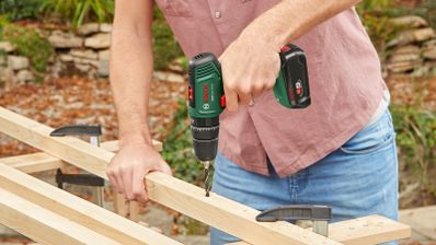 Taladro Bosch EasyImpact 18V-40 perforando un listón de madera sujeto a un banco de trabajo.