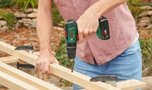 Taladro Bosch EasyImpact 18V-40 perforando un listón de madera sujeto a un banco de trabajo.