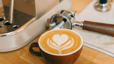 Taza de café cremoso junto a una cafetera espresso.