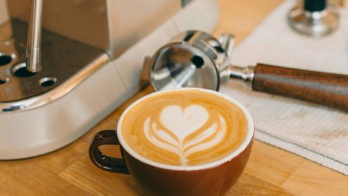 Taza de café cremoso junto a una cafetera espresso.