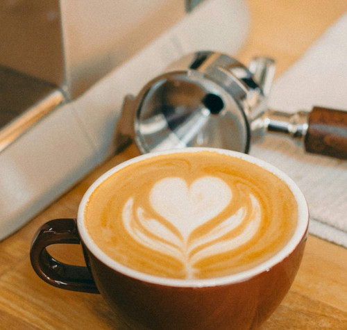 Taza de café cremoso junto a una cafetera espresso.