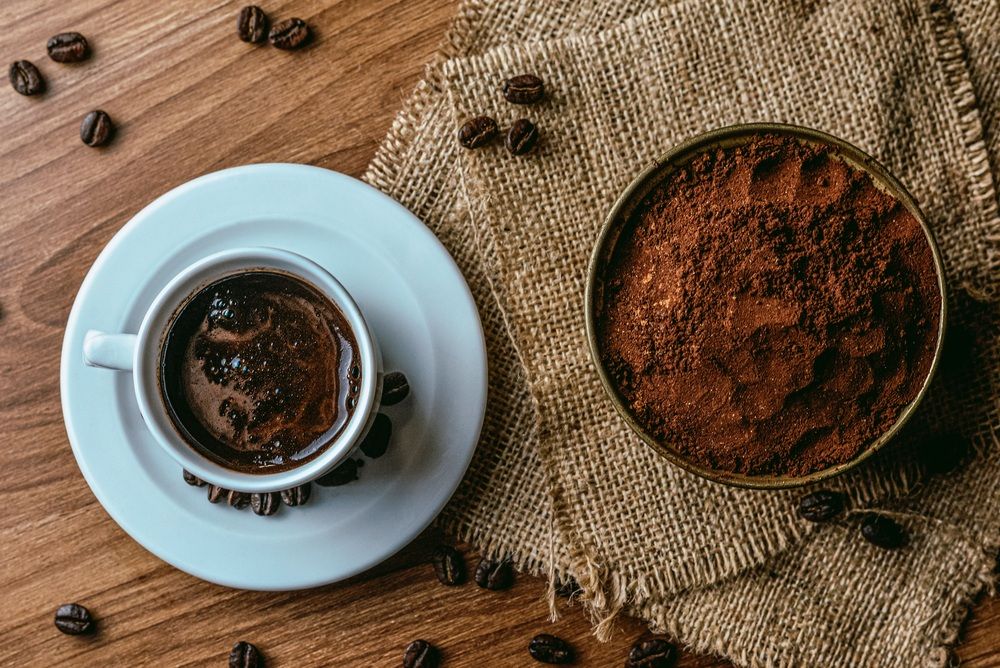 Vista cenital de una taza blanca con café negro rodeada de granos tostados.