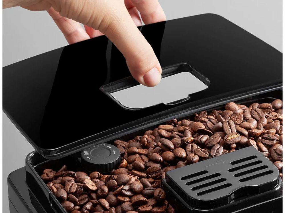 Mano levantando la tapa del depósito de café en grano de una cafetera De’Longhi.