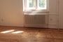 Radiador blanco bajo una ventana en una habitación con suelo de madera y luz natural.